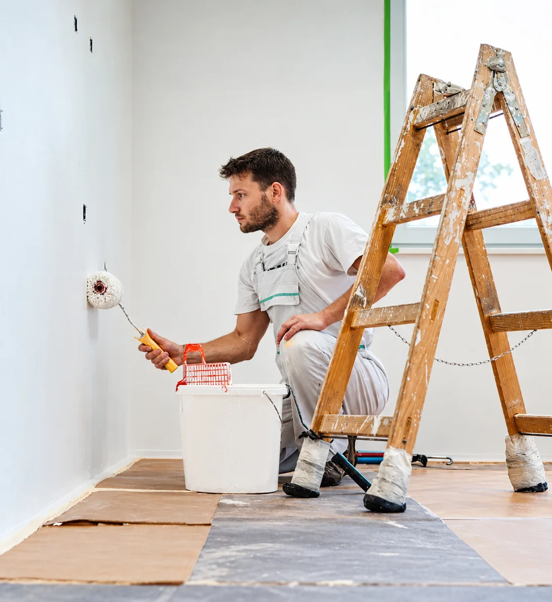 Artisan peintre au rouleau dans une pièce avec le sol protégé